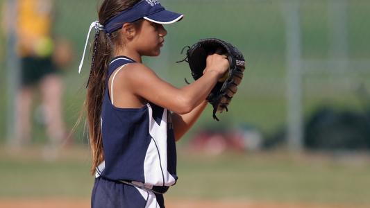young girl in baseball uniform about to pitch